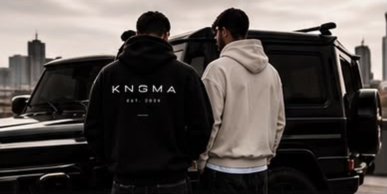 Twee mannen in een zwarte en een zandkleurige KNGMA-hoodie bij een zwarte terreinwagen
